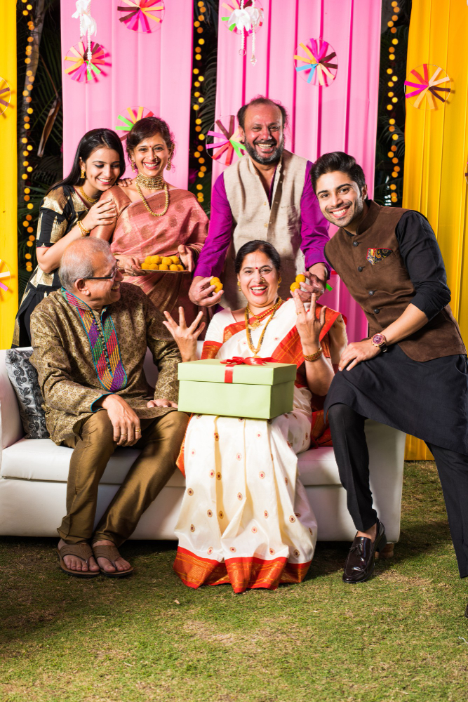 multigenerational-indian-family-eating-sweets-while-celebrating-festival-occasion-dressed-traditional-wear-sitting-sofa-couch