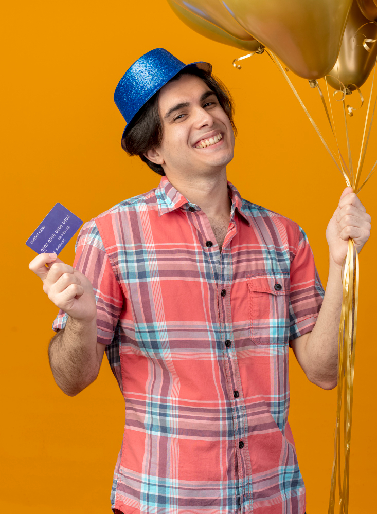 smiling-handsome-caucasian-man-wearing-blue-party-hat-holds-helium-balloons-credit-card-looking-camera